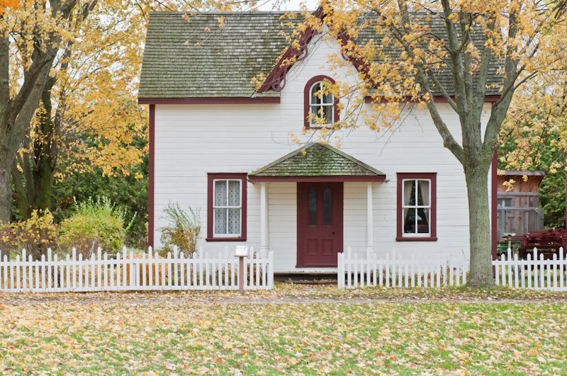 White two-story house with a red front door and a white picket fence