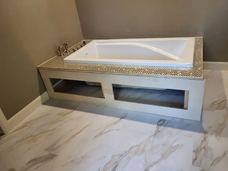 Drop-in tub set in a built deck topped with gold penny tile, framing still open below