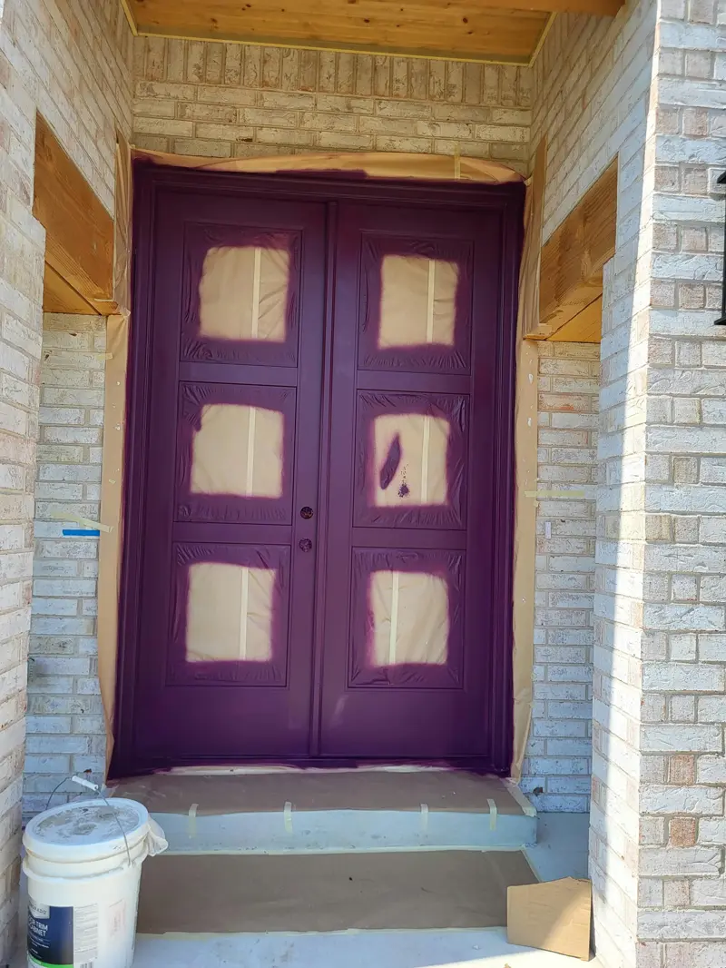 Double front doors freshly painted plum with the surrounding brick masked off