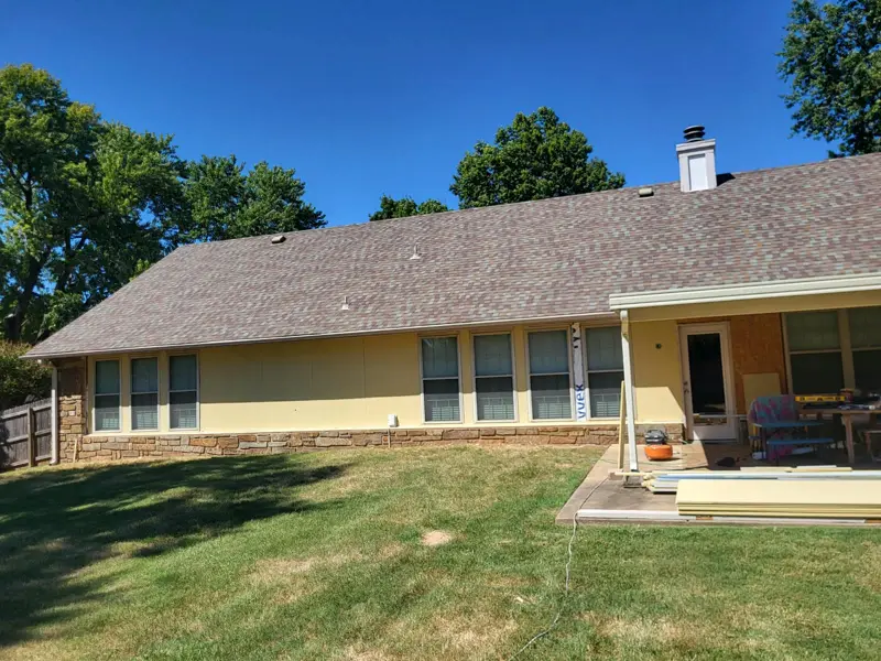 Back of a ranch-style home with new siding going up above a stone wainscot
